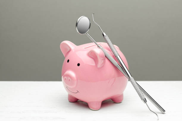 Pink piggy bank with dental tools on gray background, illustrating saving money on dental treatment